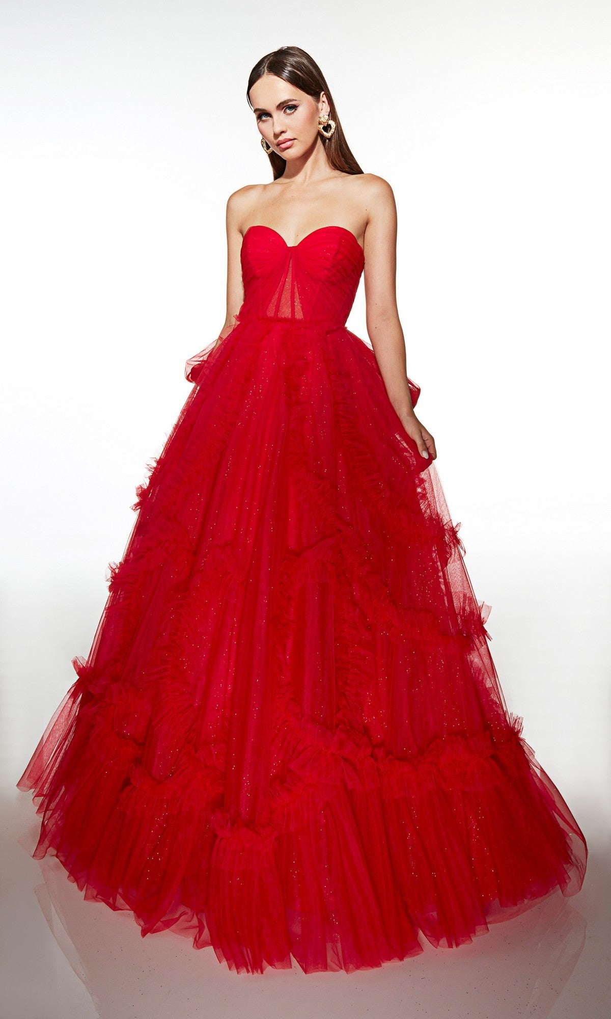 A woman stands against a plain white background wearing the Alyce 62119 long prom dress, featuring a strapless fitted corset bodice and a voluminous bright red tulle ruffled skirt.